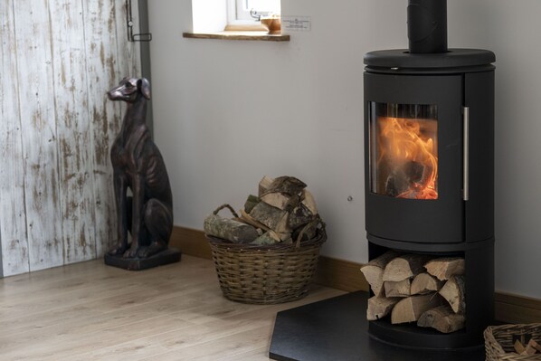 A room with a black wood-burning stove, a dog statue, and a basket of firewood.