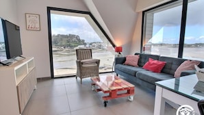 A modern living room with a large window, a sofa, a chair, a coffee table, and a TV on a cabinet.
