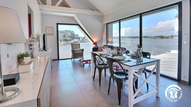 A modern dining area with a view of the sea, a large window, and a dining table set with plates and glasses.