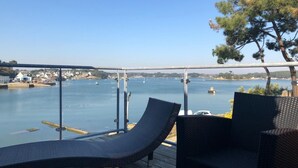 A balcony with two lounge chairs overlooking a body of water with boats and a distant shoreline.