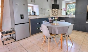 A modern kitchen with a built-in refrigerator, a dining table with chairs, and a window with a view of greenery. - Mazibihan - LIMERZEL (LIMERZEL)