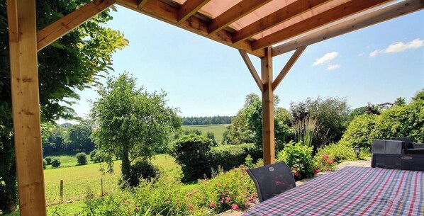 A wooden pergola structure with a table and chairs, overlooking a green landscape with trees and a field. - Mazibihan - LIMERZEL (LIMERZEL)