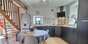 A modern kitchen with dark cabinets, a built-in stove, and a dining area with a table and chairs. - Mazibihan - LIMERZEL (LIMERZEL)