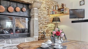 A cozy room with a stone fireplace, a wooden table with tea set, and a bookshelf with books. - Mazibihan - LIMERZEL (LIMERZEL)