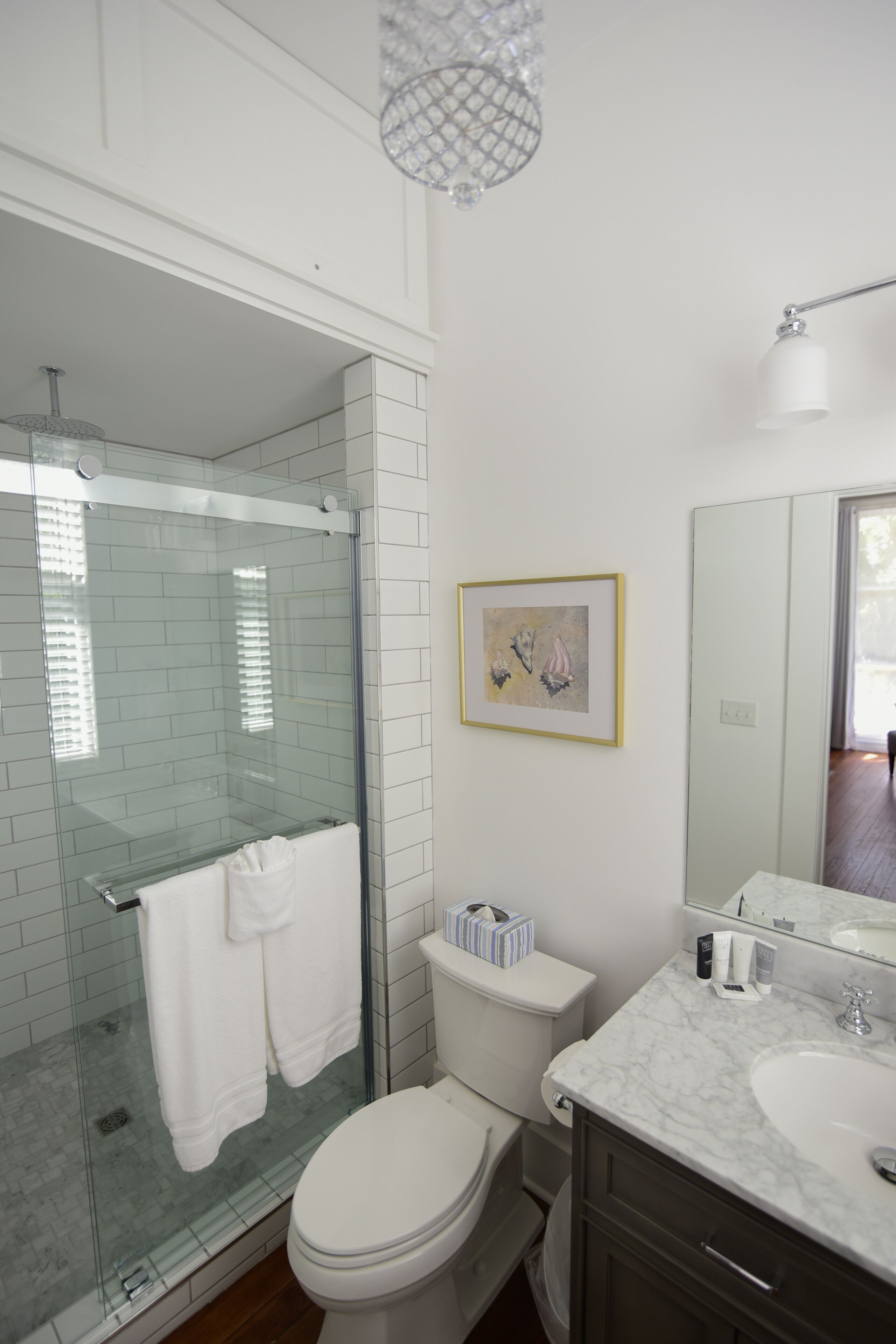 Ein modernes Badezimmer mit einer Glaskabine zur Dusche, einer weißen Toilette, einem мраморном Waschbecken und einem gerahmten Kunstwerk an der Wand.