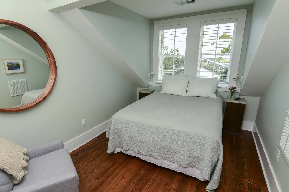 Un dormitorio con cama, mesita de noche, espejo y ventana con persianas.
