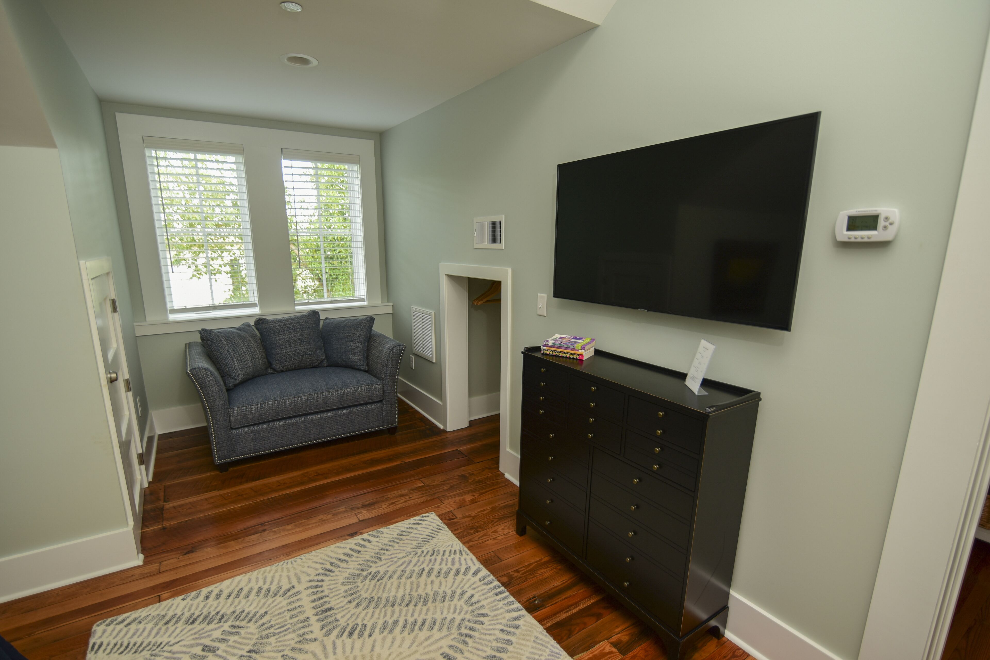 Una sala de estar con piso de madera oscura, un sofá gris, un mueble de entretenimiento negro y un televisor de pantalla plana montado en la pared.