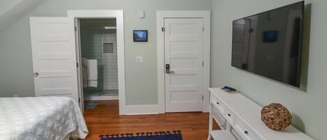 Un dormitorio con cama, televisor, cómoda blanca y puerta que da a un baño.