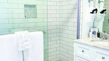 A modern bathroom with white tiled walls, a glass shower enclosure, a white vanity with drawers, and a large mirror.