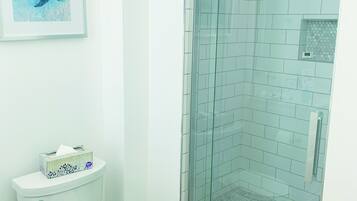 A bathroom with a toilet, a glass-enclosed shower, and a framed picture on the wall.