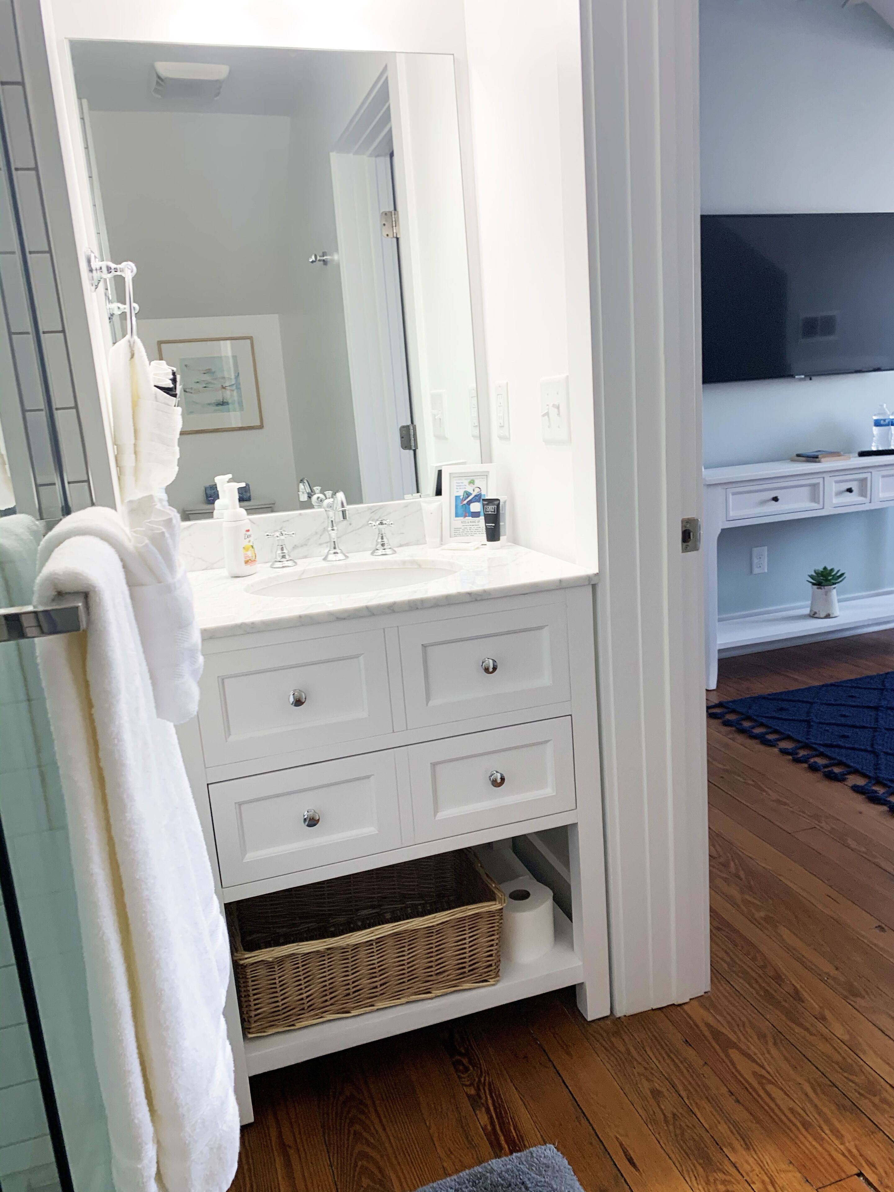 A bathroom with a white vanity, a large mirror, and a towel rack.