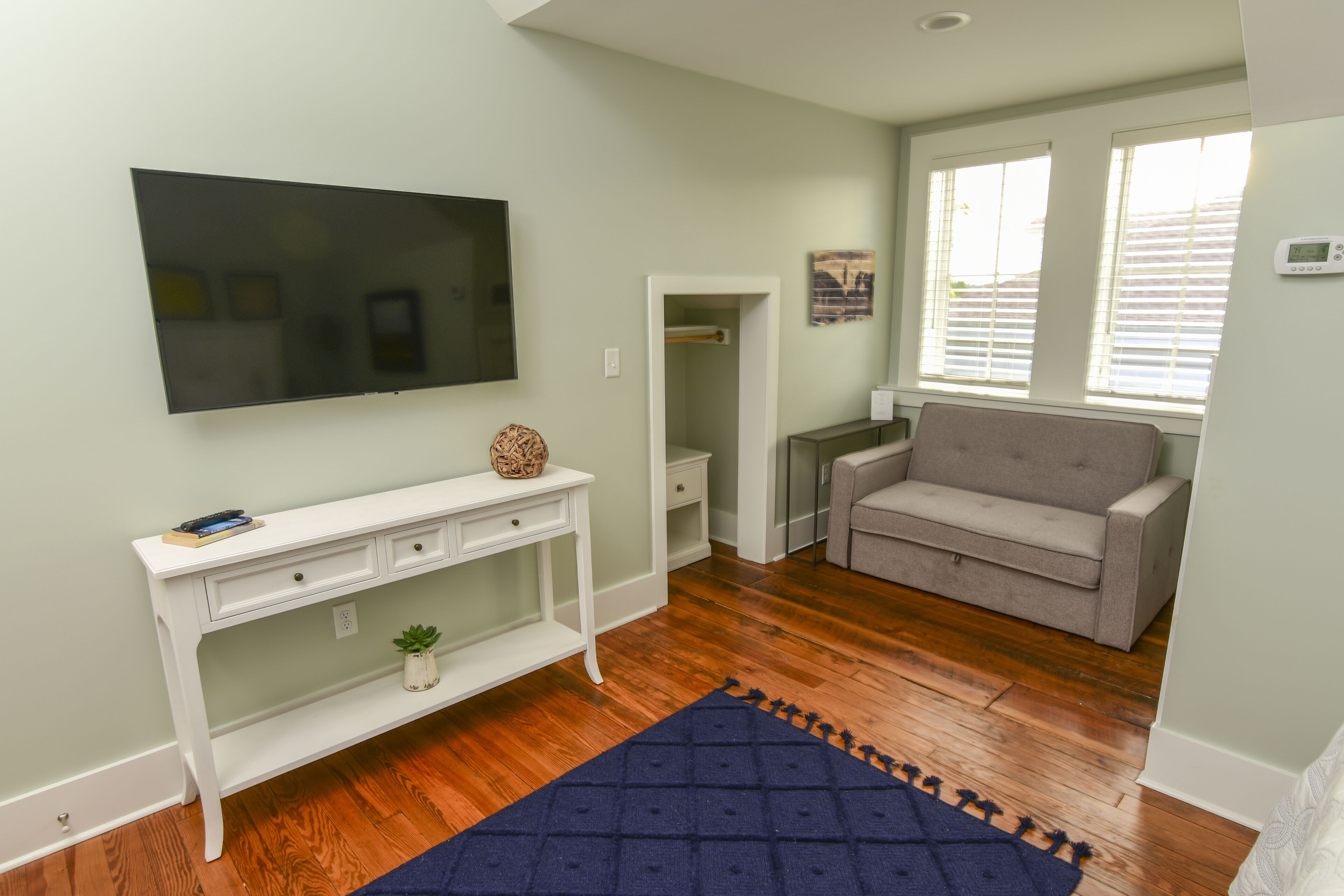 A living room with a flat-screen TV, a white console table, a grey sofa, and a blue rug.