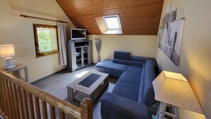 Un salon chaleureux, aménagé dans un style industriel, avec un plafond en bois, une grande fenêtre, un téléviseur, un canapé et une table basse.