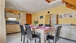 Une cuisine moderne avec des meubles en bois, un coin repas avec une table dressée pour quatre personnes et une horloge au mur.