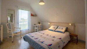 A bedroom with a bed, a chair, a small table, a window, and a ceiling light. - Les Filets de la Ria (BELZ)