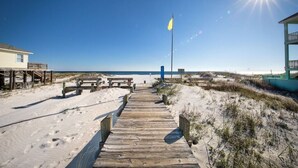 En träpromenad som leder till en strand med en flaggstång och en byggnad med en balkong.