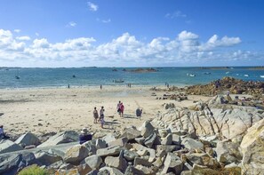 Een rotsachtig strand met mensen die wandelen en boten in het water.