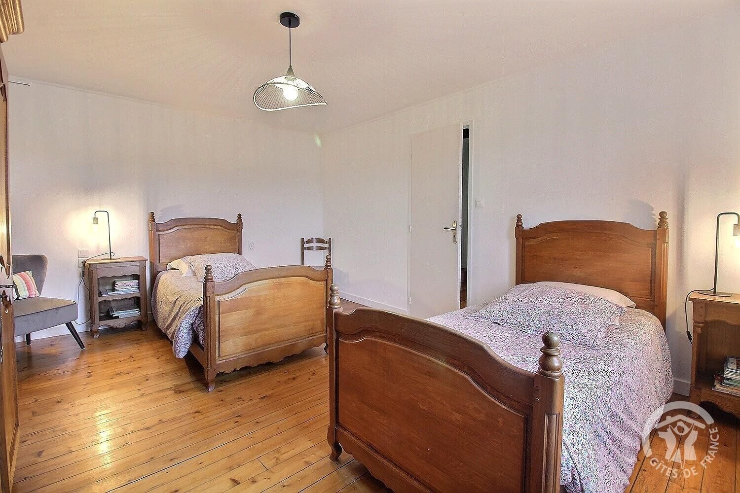 A bedroom with two wooden beds, a bedside table, a chair, a wardrobe, and a hanging light fixture.