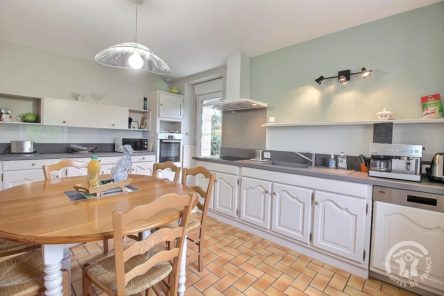 A modern kitchen with white cabinetry, a wooden dining table, and a built-in oven.