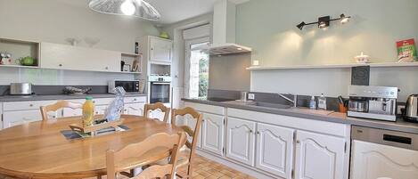 A modern kitchen with white cabinetry, a wooden dining table, and a built-in oven.