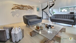 Una sala de estar moderna con dos sofás grises, una mesa de centro de vidrio y una escalera espiral.