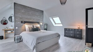 Un dormitorio moderno con cama, mesitas de noche, cómoda, tragaluz y lámpara colgante.
