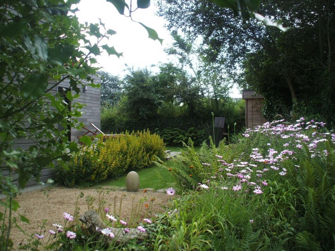 A garden with various plants and flowers, a stone sculpture, and a wooden fence.