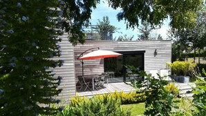 Une terrasse extérieure moderne, dotée d’une table et de chaises, et entourée d’une végétation luxuriante et de plantes en fleurs.