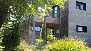 Un bâtiment moderne à deux étages, doté d’un balcon et entouré d’une végétation luxuriante.