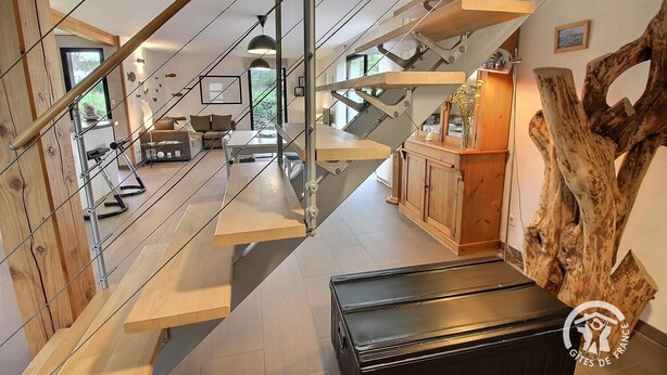 Un intérieur moderne avec un escalier menant à une mezzanine, agrémenté d’une armoire en bois et d’une grande sculpture représentant un tronc d’arbre.