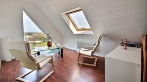 A modern room with a sloped ceiling, a glass table, two chairs, a radiator, and a view of the city.