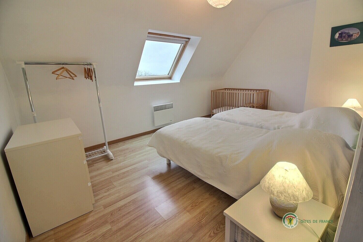 A bedroom with a bed, a nightstand, a radiator, a window, and a wardrobe.