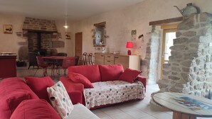 Un salon chaleureux avec un canapé rouge, une table à manger avec des chaises et un coin cuisine doté d’un mur en pierre.
