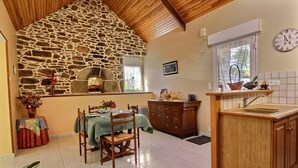 Una cocina rústica con pared de piedra, armarios de madera y un comedor con mesa para dos.