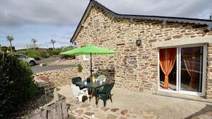 Un edificio de piedra con un patio que tiene una mesa, sillas, una sombrilla verde y un coche aparcado cerca.