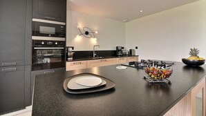 Une cuisine moderne avec des meubles de couleur sombre, un plan de travail noir et un panier de fruits.