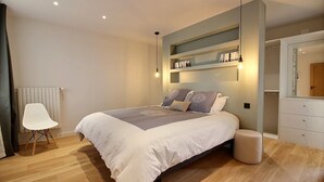 Une chambre moderne avec un grand lit, une table de chevet, une chaise, une commode et une bibliothèque intégrée.