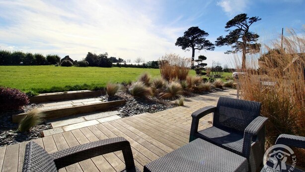 Une terrasse en bois avec des meubles en osier et, en arrière-plan, un champ d’herbe.