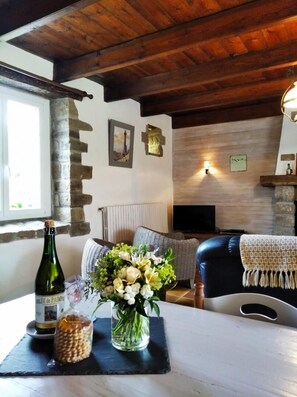 Un salon chaleureux avec une cheminée en pierre, un téléviseur et une table sur laquelle se trouvent une bouteille et des fleurs.