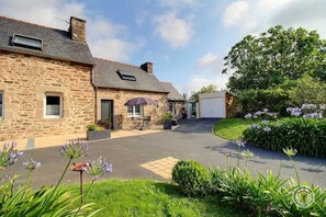 A stone building with a paved driveway, a covered outdoor seating area, and a garage.