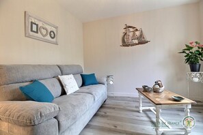 A living room with a grey sofa, a wooden coffee table, a small side table, a wall-mounted ship decoration, and a framed picture with heart shapes. - Penty - YVIAS - Gîte (YVIAS)