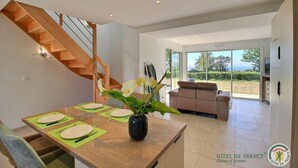 A modern interior with a wooden dining table set for four, a staircase, a sofa, and a TV.
