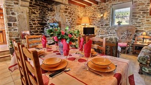 Un coin repas aux murs de pierre, avec une table dressée pour deux personnes, agrémentée d’assiettes oranges et d’un vase de fleurs.