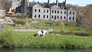 Un bâtiment historique en pierre, doté d’une grande fenêtre et d’un mur de pierre à l’avant.