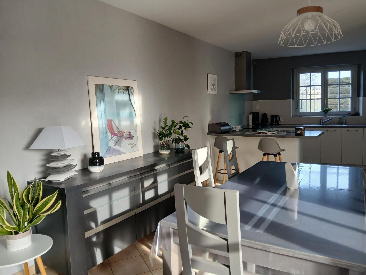 Une cuisine moderne avec un coin repas, comprenant un grand îlot central, des chaises, une table et un luminaire suspendu.