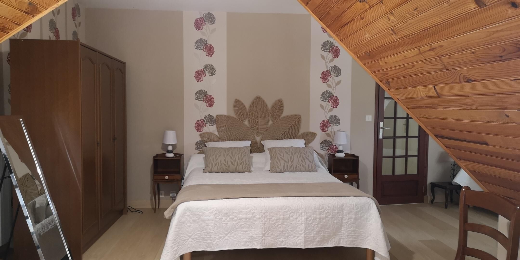 A bedroom with a bed, two nightstands, a wooden wardrobe, and a floral wall decoration.