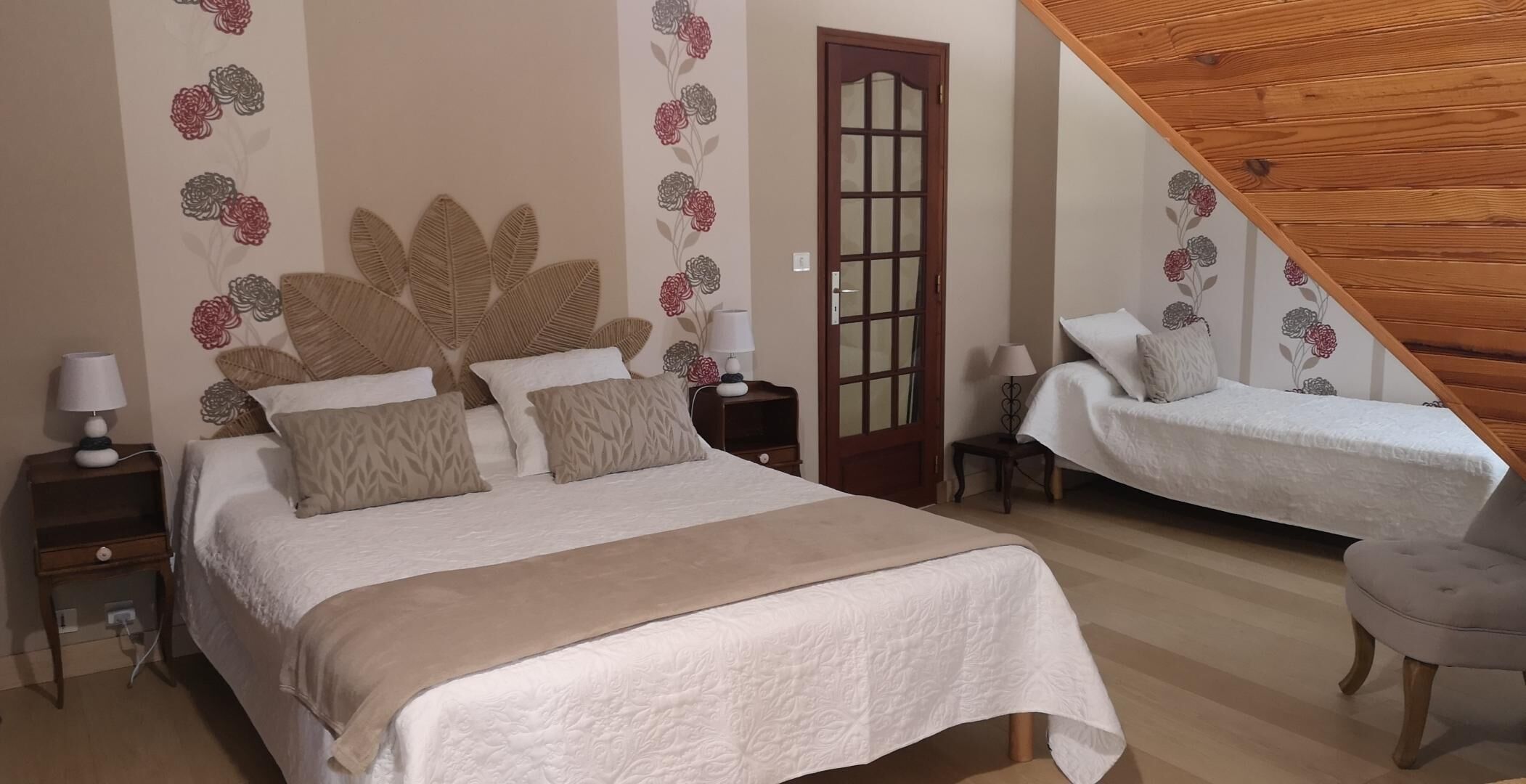Un dormitorio con dos camas, techo de madera y decoración floral en las paredes.