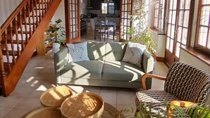 Amplia sala de estar con techo alto, vigas de madera, una escalera, un sofá, dos pequeñas mesas redondas y un sillón estampado.