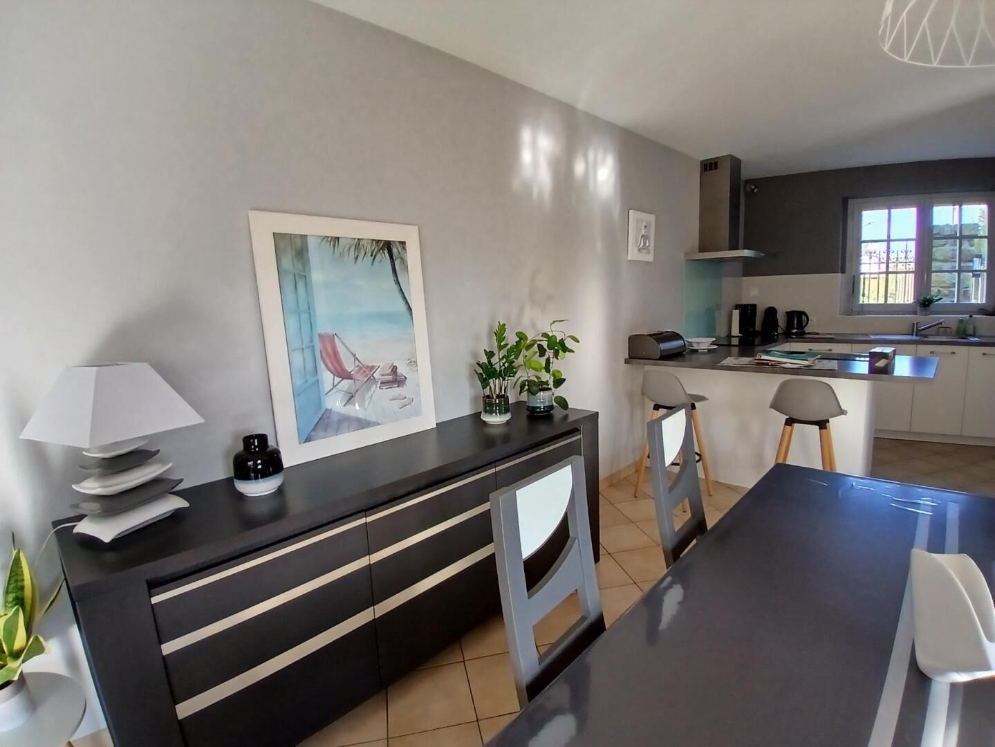 Une cuisine moderne avec un coin repas, comprenant un grand îlot central, des tabourets de bar et une vue sur l’extérieur.