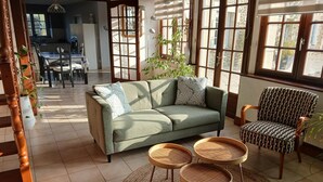 Una sala de estar acogedora con un sofá, dos mesitas auxiliares y un sillón estampado.